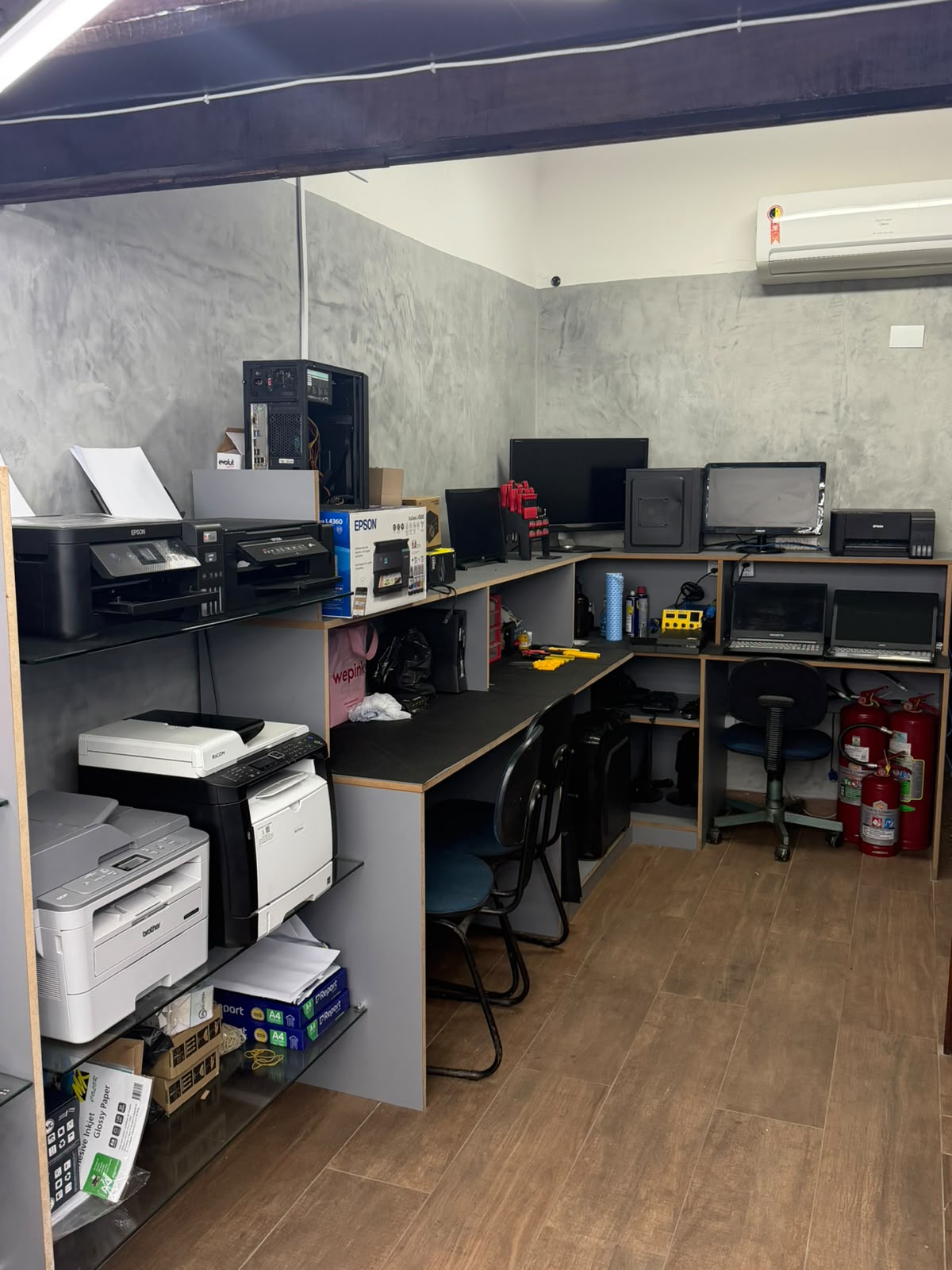 Bancada técnica da Sampaio TechLAB com computadores, notebooks, impressoras e ferramentas de manutenção