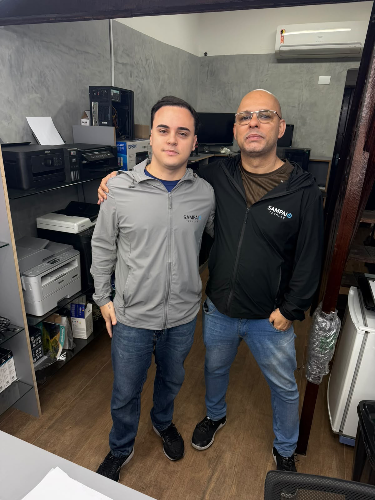 Equipe da Sampaio TechLAB uniformizada na loja, com impressoras e computadores em manutenção ao fundo